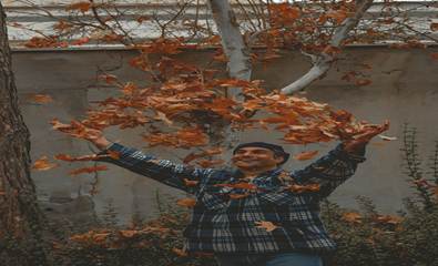 Man joyfully tossing autumn leaves in the air on a windy day, celebrating fall colors.