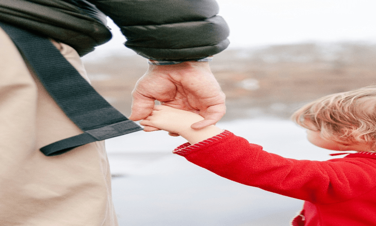 Father and child holding hands outdoors, symbolizing warmth, safety, and understanding.
